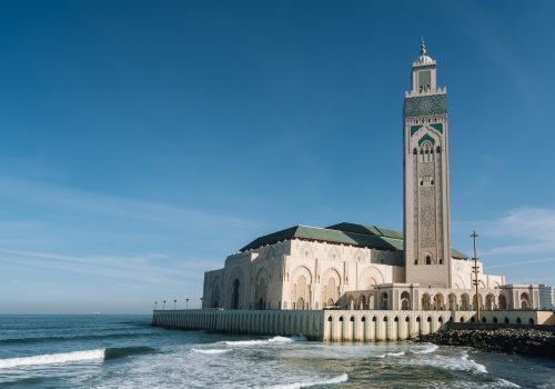 Hassan II Mosque surrounded by water and buildings under a blue sky and sunlight