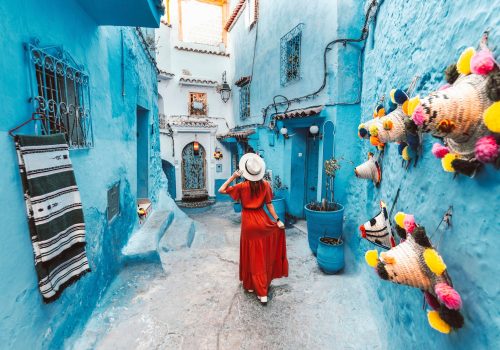 Young woman with red dress visiting the blue city Chefchaouen, Marocco